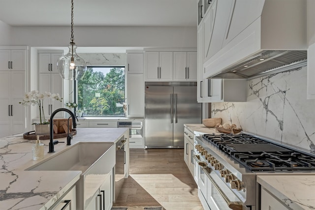 kitchen with light stone countertops, custom range hood, pendant lighting, wood-type flooring, and high quality appliances