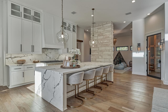 kitchen with backsplash, light stone countertops, white cabinets, and light wood-type flooring