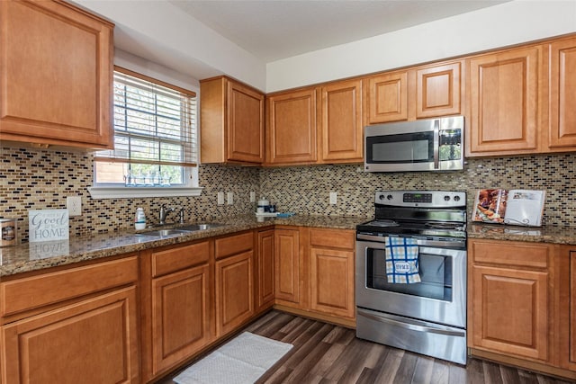 kitchen with sink, decorative backsplash, dark stone countertops, appliances with stainless steel finishes, and dark hardwood / wood-style flooring