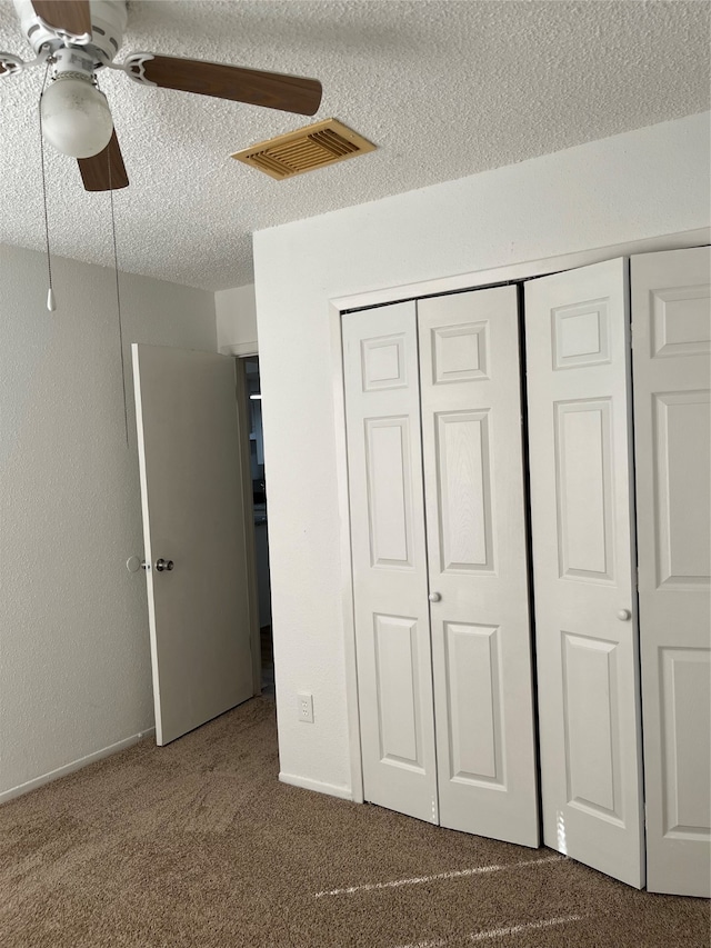 unfurnished bedroom with carpet flooring, ceiling fan, a textured ceiling, and a closet