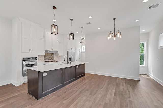 kitchen featuring stainless steel appliances, decorative light fixtures, an inviting chandelier, hardwood / wood-style flooring, and a center island with sink