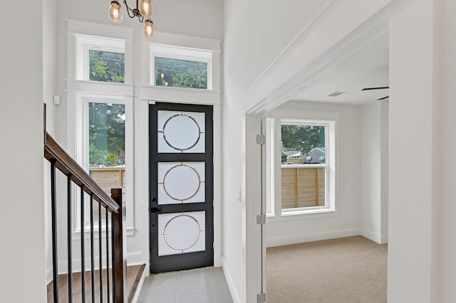 carpeted entrance foyer with ceiling fan with notable chandelier and a healthy amount of sunlight