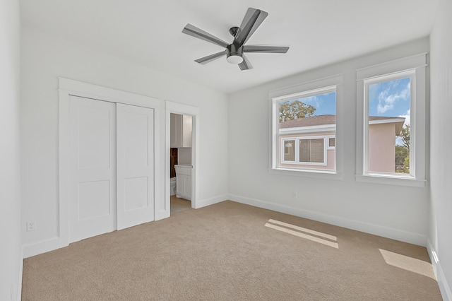 unfurnished bedroom with a closet, light colored carpet, ceiling fan, and connected bathroom