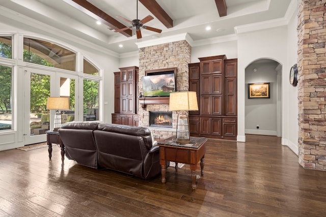 living area featuring arched walkways, a towering ceiling, dark wood-style flooring, beamed ceiling, and a fireplace