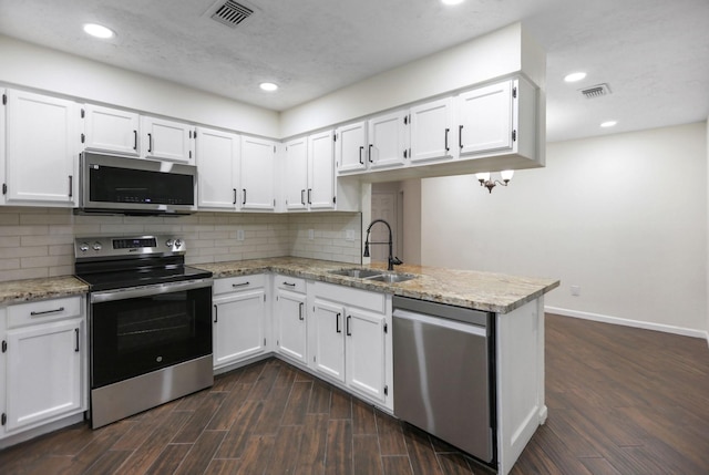 kitchen with light stone counters, dark hardwood / wood-style flooring, kitchen peninsula, stainless steel appliances, and white cabinets