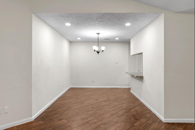 unfurnished dining area with dark hardwood / wood-style flooring, a textured ceiling, and a chandelier