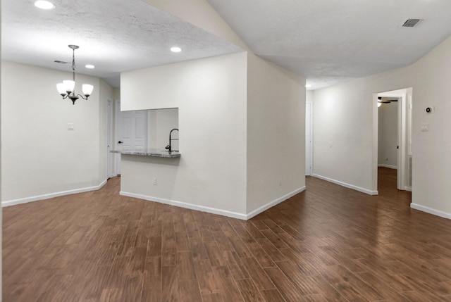 unfurnished living room with an inviting chandelier, dark hardwood / wood-style flooring, sink, and a textured ceiling