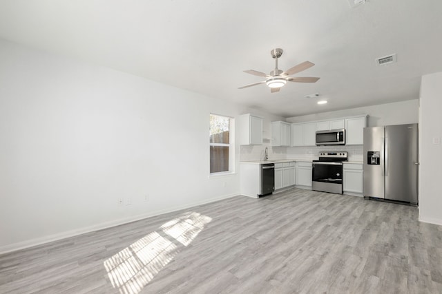 kitchen featuring white cabinets, ceiling fan, light wood-type flooring, appliances with stainless steel finishes, and tasteful backsplash