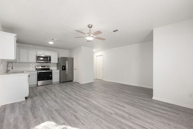 kitchen with white cabinets, appliances with stainless steel finishes, backsplash, and light hardwood / wood-style flooring