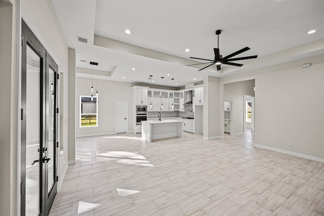 unfurnished living room with ceiling fan, sink, and a tray ceiling