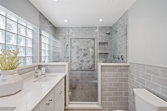 bathroom with vanity, toilet, a shower with shower door, and tile walls