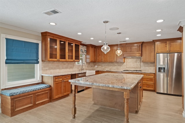 kitchen with a center island, light stone countertops, appliances with stainless steel finishes, decorative light fixtures, and light hardwood / wood-style floors