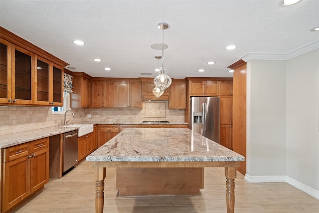 kitchen with appliances with stainless steel finishes, crown molding, sink, a center island, and hanging light fixtures