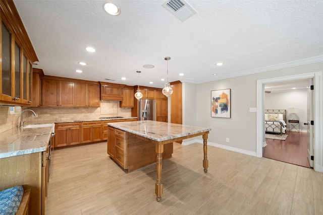 kitchen with hanging light fixtures, stainless steel appliances, light hardwood / wood-style floors, a kitchen island, and ornamental molding