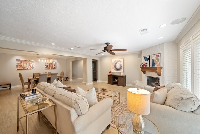 living room featuring a fireplace, a textured ceiling, ceiling fan, and ornamental molding