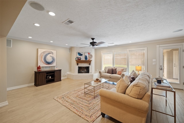 living room featuring a fireplace, a textured ceiling, light hardwood / wood-style flooring, and ceiling fan