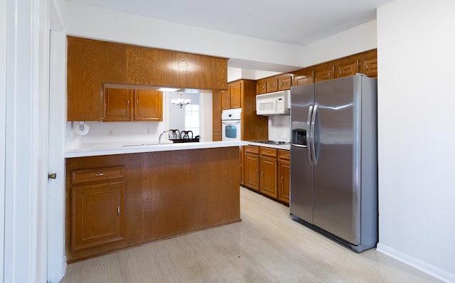 kitchen with kitchen peninsula, a chandelier, pendant lighting, white appliances, and light wood-type flooring