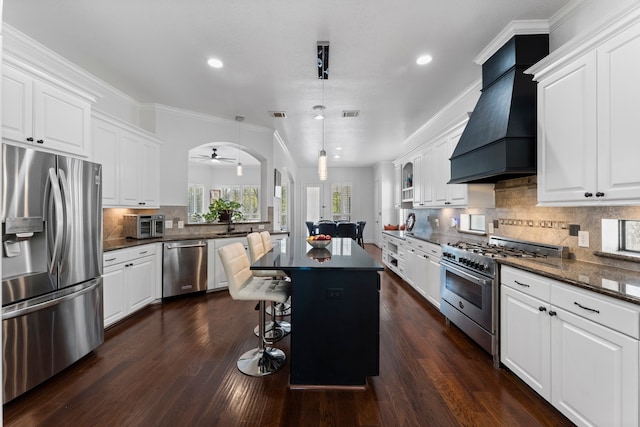 kitchen featuring pendant lighting, white cabinets, a center island, stainless steel appliances, and premium range hood