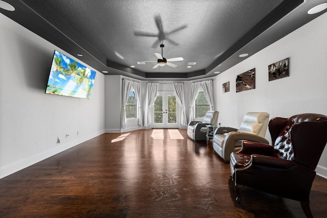 living area with ceiling fan, french doors, a raised ceiling, hardwood / wood-style flooring, and a textured ceiling