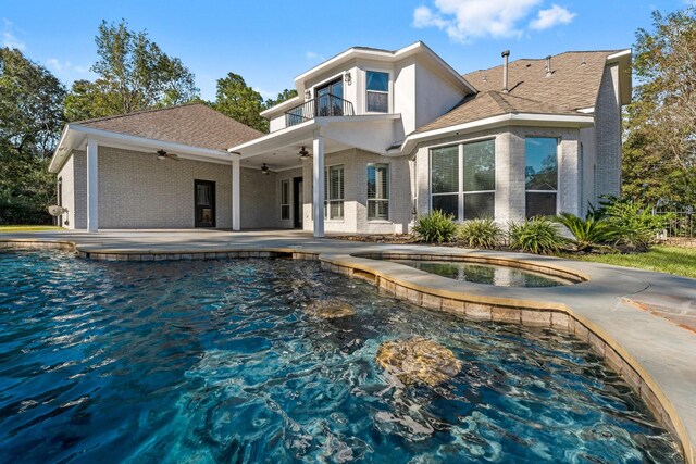 back of house featuring ceiling fan, a patio area, a pool with hot tub, and a balcony