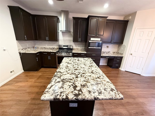 kitchen featuring wall chimney exhaust hood, stainless steel gas range oven, hardwood / wood-style floors, decorative backsplash, and a kitchen island