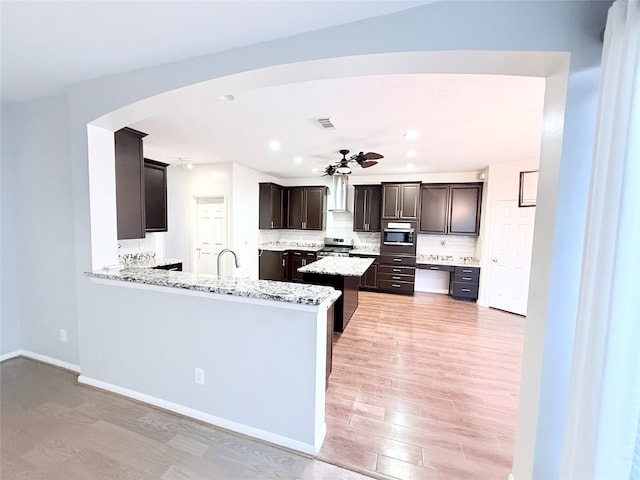 kitchen featuring kitchen peninsula, light wood-type flooring, backsplash, stainless steel appliances, and ceiling fan