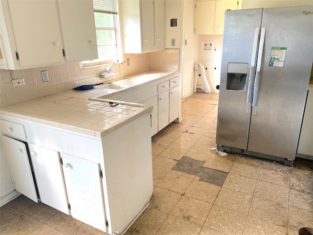 kitchen with backsplash, tile counters, white cabinetry, and stainless steel refrigerator with ice dispenser