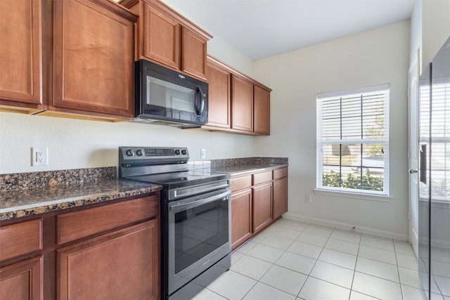 kitchen featuring light tile patterned floors, dark stone counters, and stainless steel range with electric cooktop