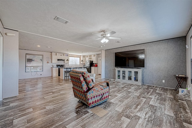 living room featuring ceiling fan, a textured ceiling, and light hardwood / wood-style flooring