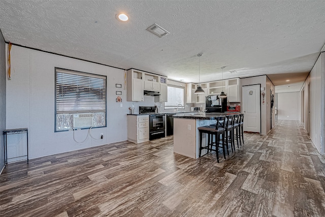 kitchen featuring a breakfast bar, black appliances, white cabinets, hanging light fixtures, and a kitchen island