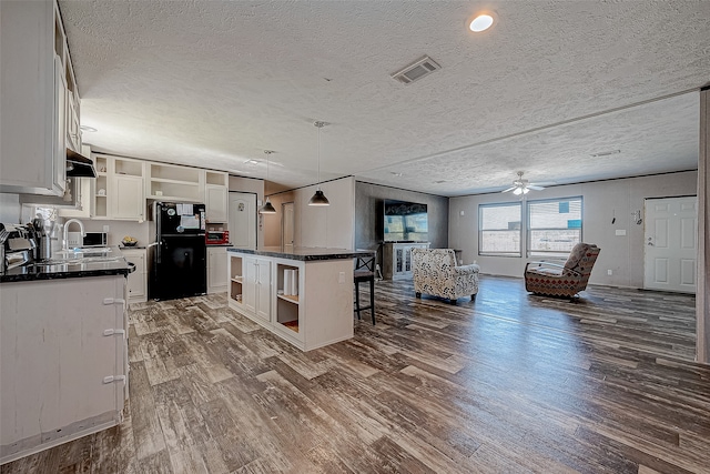 kitchen with black fridge, a textured ceiling, decorative light fixtures, white cabinets, and a center island