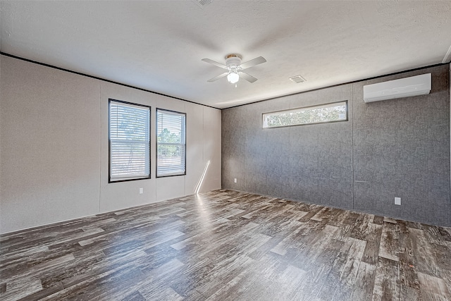 unfurnished room featuring dark hardwood / wood-style flooring, a textured ceiling, a wealth of natural light, and a wall mounted AC