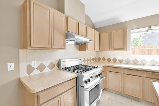 kitchen featuring light brown cabinetry, backsplash, vaulted ceiling, light tile patterned floors, and high end stainless steel range