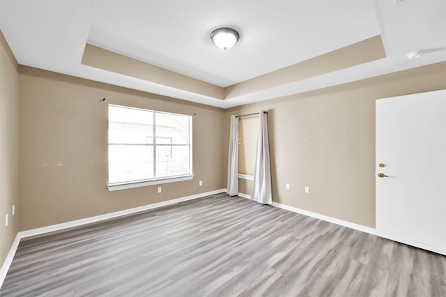 empty room featuring a raised ceiling and light hardwood / wood-style floors