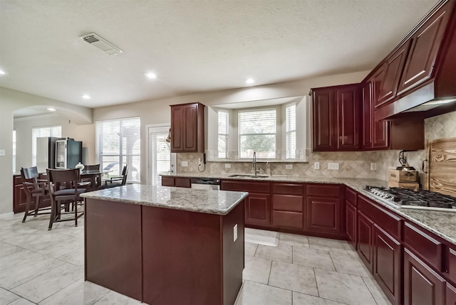 kitchen with backsplash, sink, appliances with stainless steel finishes, a kitchen island, and light stone counters