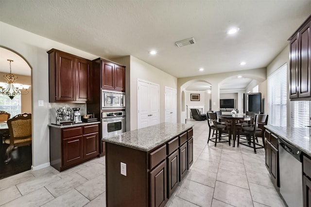 kitchen with light stone counters, a chandelier, decorative light fixtures, a kitchen island, and appliances with stainless steel finishes