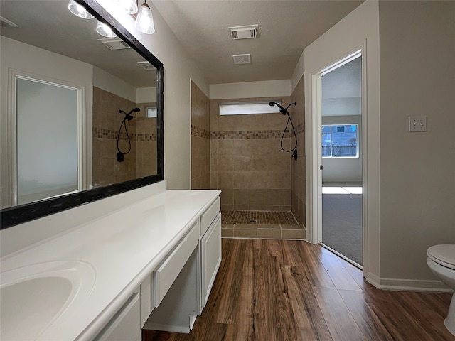 bathroom featuring a tile shower, vanity, hardwood / wood-style flooring, and toilet