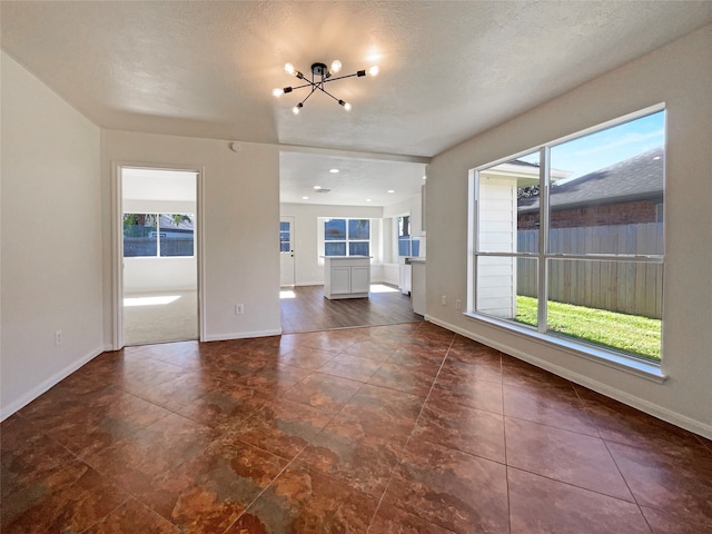 unfurnished living room featuring a healthy amount of sunlight, a textured ceiling, and a notable chandelier