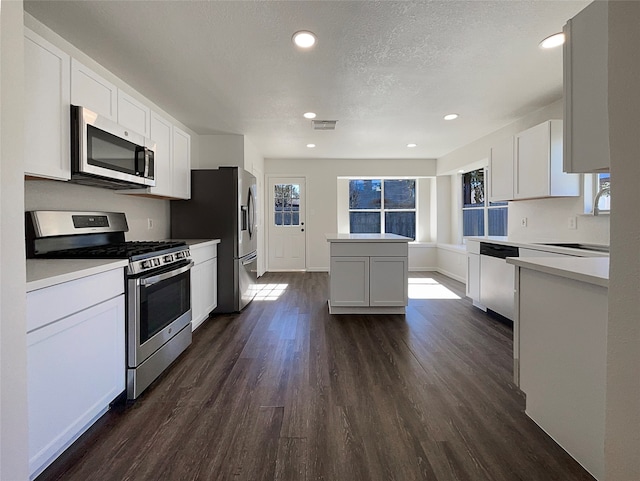 kitchen featuring a center island, dark wood-type flooring, a textured ceiling, white cabinets, and appliances with stainless steel finishes