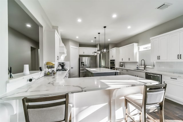 kitchen with kitchen peninsula, appliances with stainless steel finishes, sink, pendant lighting, and white cabinets