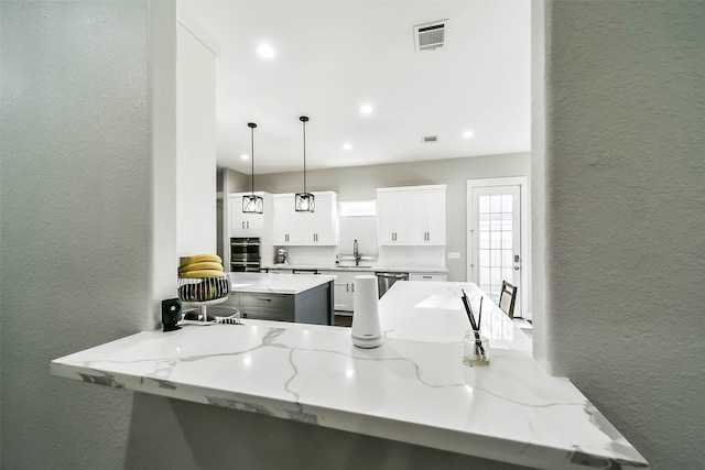 kitchen with kitchen peninsula, light stone countertops, stainless steel double oven, pendant lighting, and white cabinetry