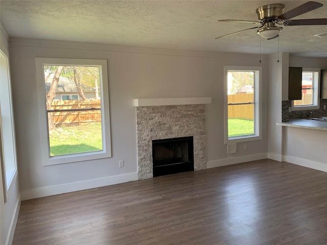 unfurnished living room featuring dark hardwood / wood-style flooring, a stone fireplace, and a textured ceiling