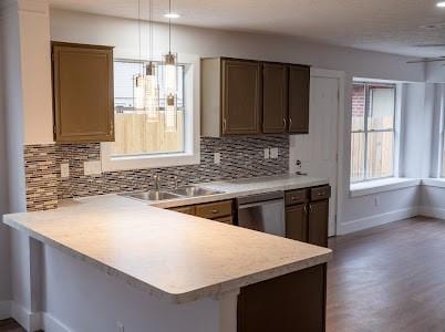 kitchen featuring tasteful backsplash, dishwasher, sink, hanging light fixtures, and kitchen peninsula