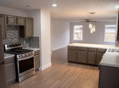 kitchen featuring stainless steel gas range, kitchen peninsula, ceiling fan, light hardwood / wood-style floors, and backsplash