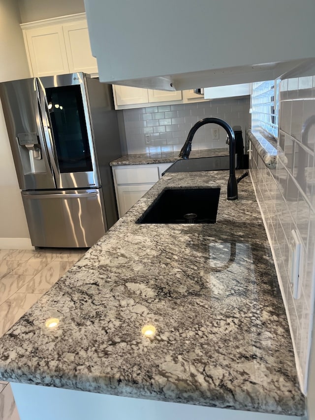 kitchen featuring tasteful backsplash, sink, stone countertops, white cabinets, and stainless steel fridge with ice dispenser