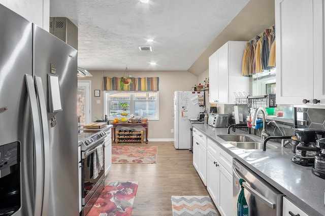 4515 Ponca St, Pasadena, TX 77504 - kitchen with appliances with stainless steel finishes, a sink, light wood finished floors, white cabinetry, and a textured ceiling