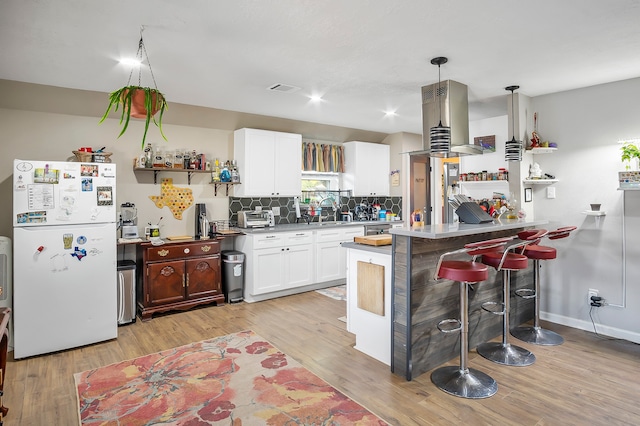 4515 Ponca St, Pasadena, TX 77504 - kitchen featuring freestanding refrigerator, a peninsula, light wood-style flooring, white cabinets, and a kitchen bar
