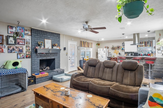 4515 Ponca St, Pasadena, TX 77504 - living area with wood finished floors, a ceiling fan, a textured ceiling, a brick fireplace, and recessed lighting