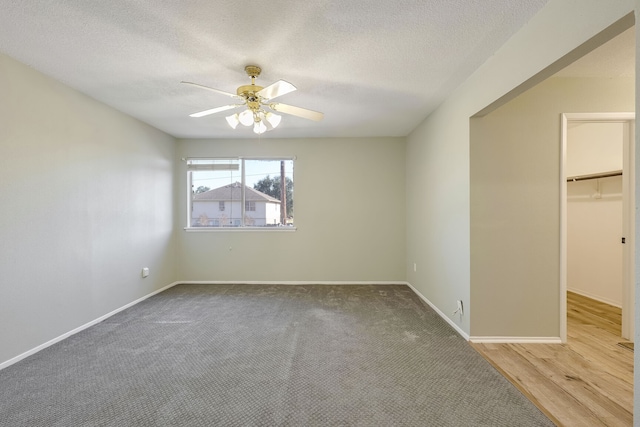 unfurnished bedroom with ceiling fan, a spacious closet, a textured ceiling, and hardwood / wood-style flooring