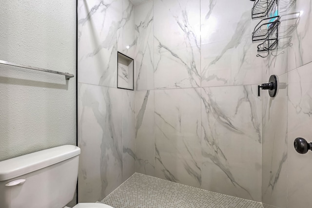 bathroom with a tile shower and toilet